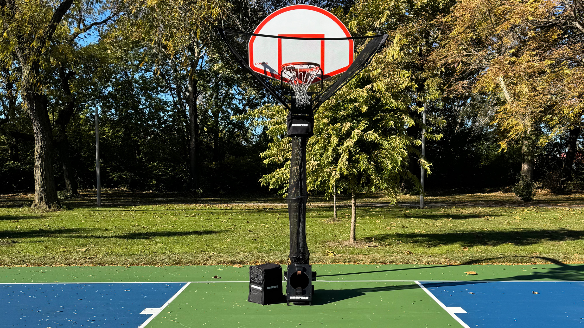 HOOPTEQ setup with backpack and basketball hoop on a court with trees in the background