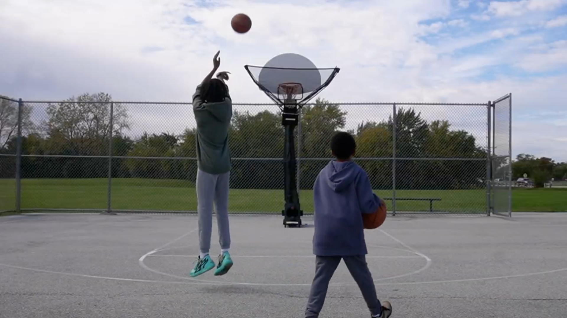 Two young hoopers playing basketball on an outdoor court with a clear sky.