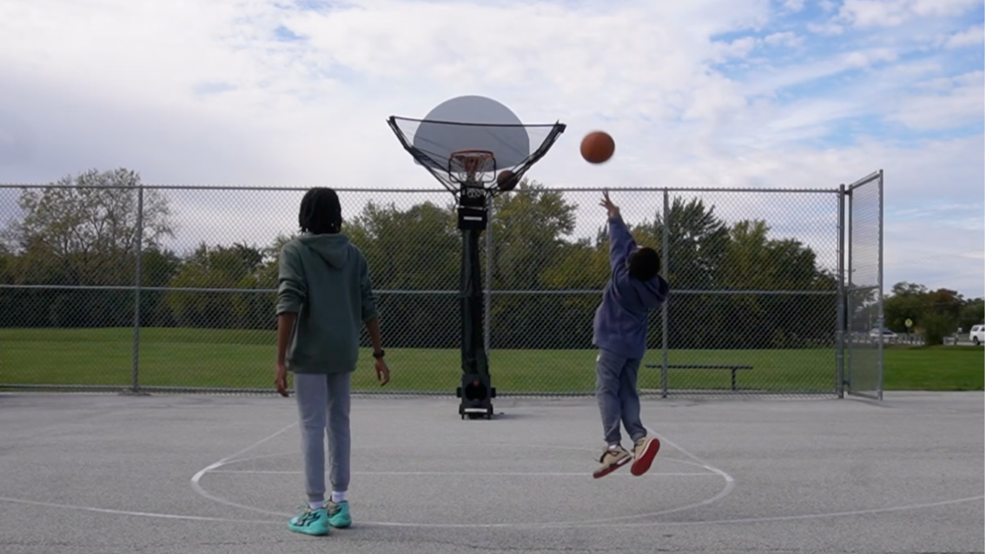 Two people on a basketball court with a hoop and ball, one person is about to shoot the ball with HOOPTEQ